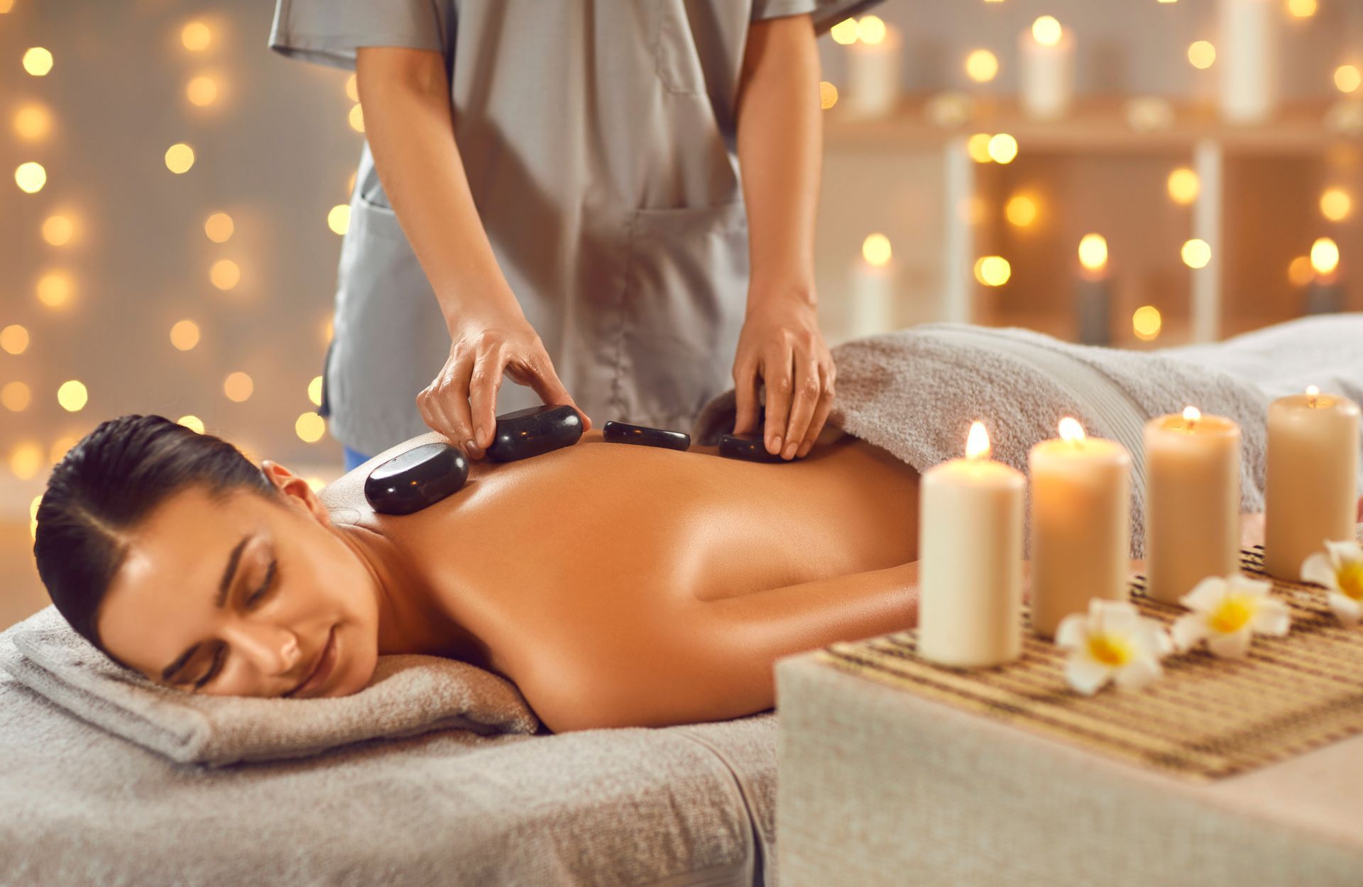 Spa massage with hot stones on a woman’s back, candles and flowers in a softly lit room