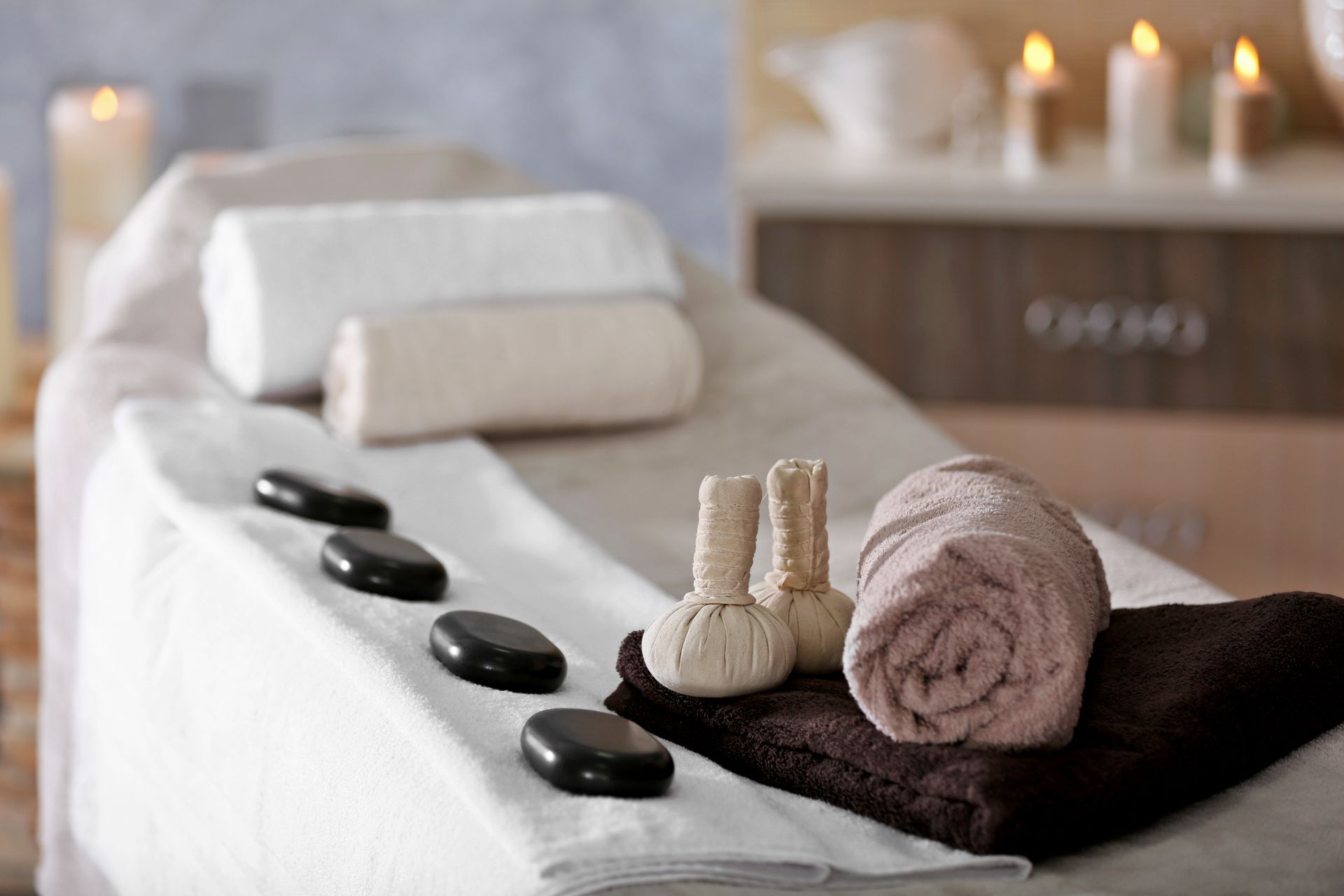 Spa massage table with rolled towels, hot stones, and candles in a calm treatment room