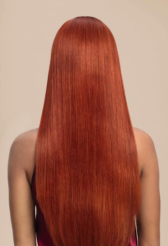 Back view of a person with long, straight copper-red hair against a beige background