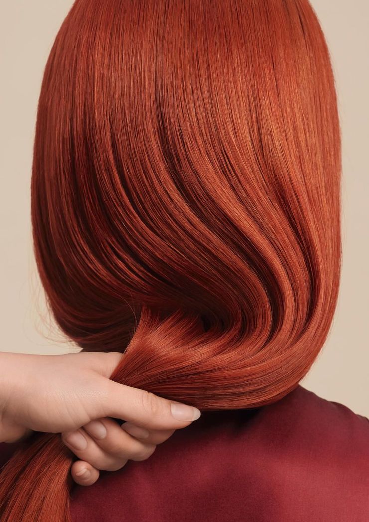 Hand holding up the ends of a sleek, shoulder-length red bob hairstyle on a maroon top