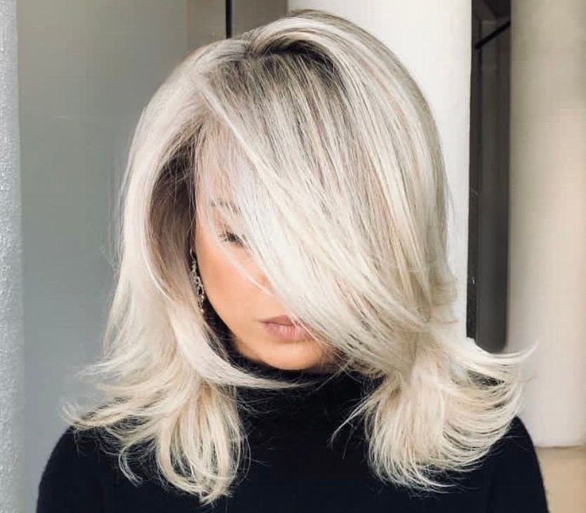 Person with platinum blonde layered hair and side-swept bangs wearing a black top against a light background