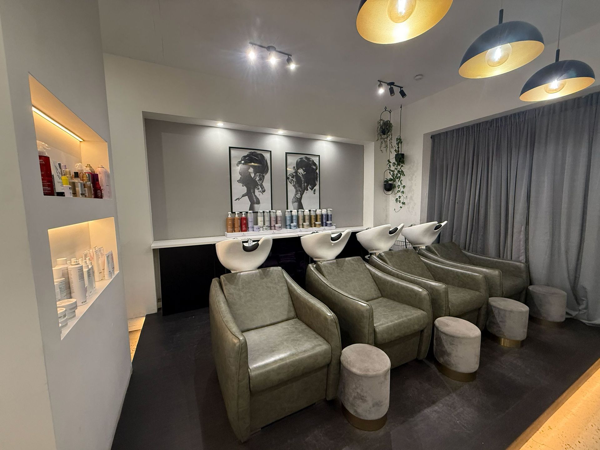 Modern lounge with olive chairs, round stools, warm pendant lights, and framed art by a window with curtains.