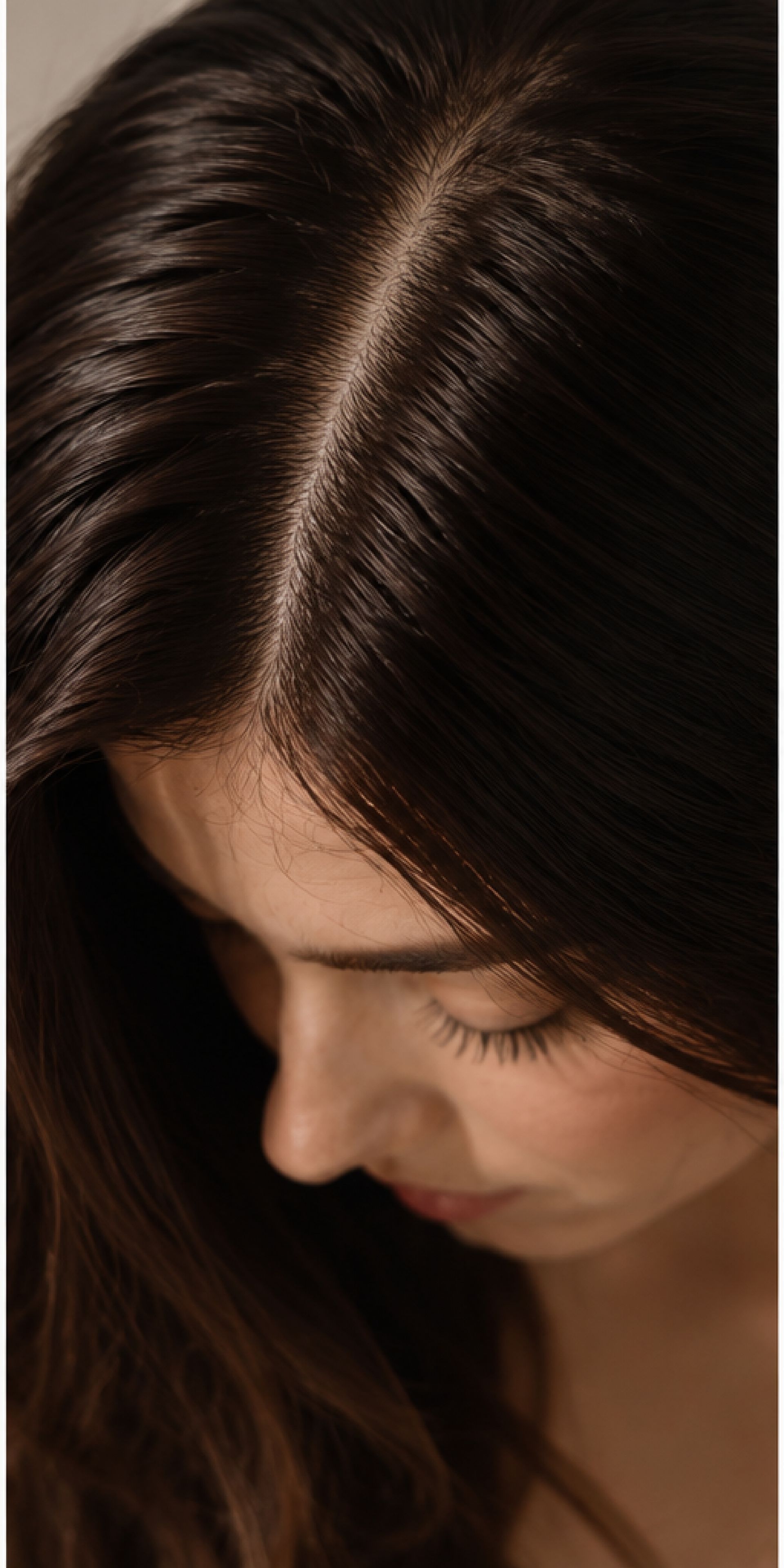 Close-up of a person with long dark brown hair, looking down against a dark background