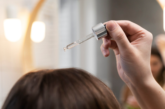 Hand holding a dropper above a person’s hair in a salon setting