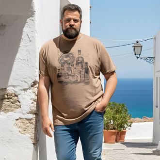 Uomo con maglietta beige e jeans in piedi accanto a un muro bianco con mare e cielo blu sullo sfondo.