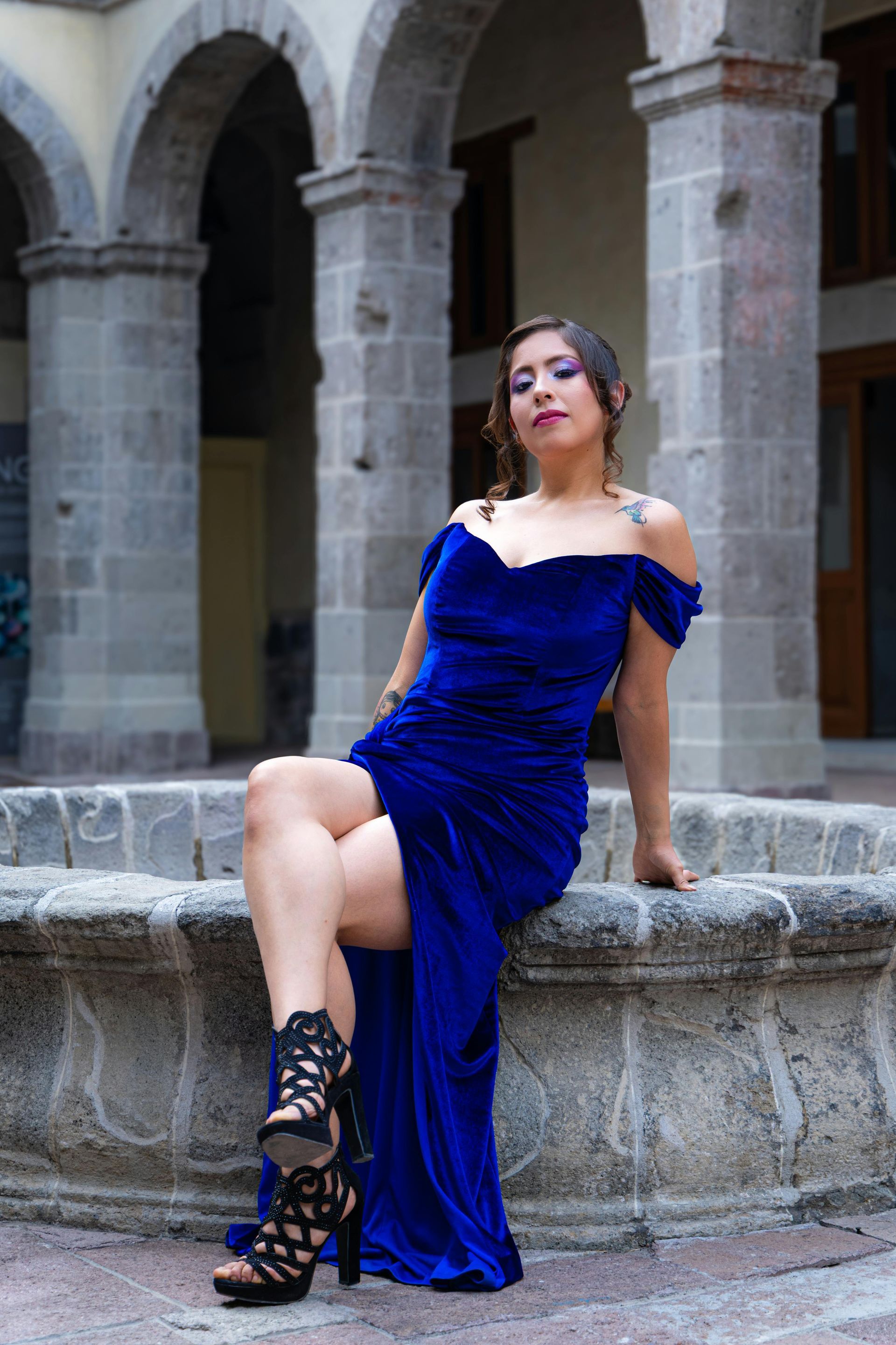 Donna in abito blu seduta su una fontana di pietra in un cortile con archi