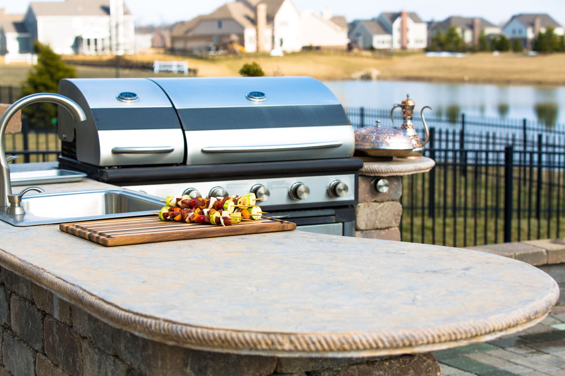 Outdoor grill and prep station with skewers on a cutting board, overlooking a pond.