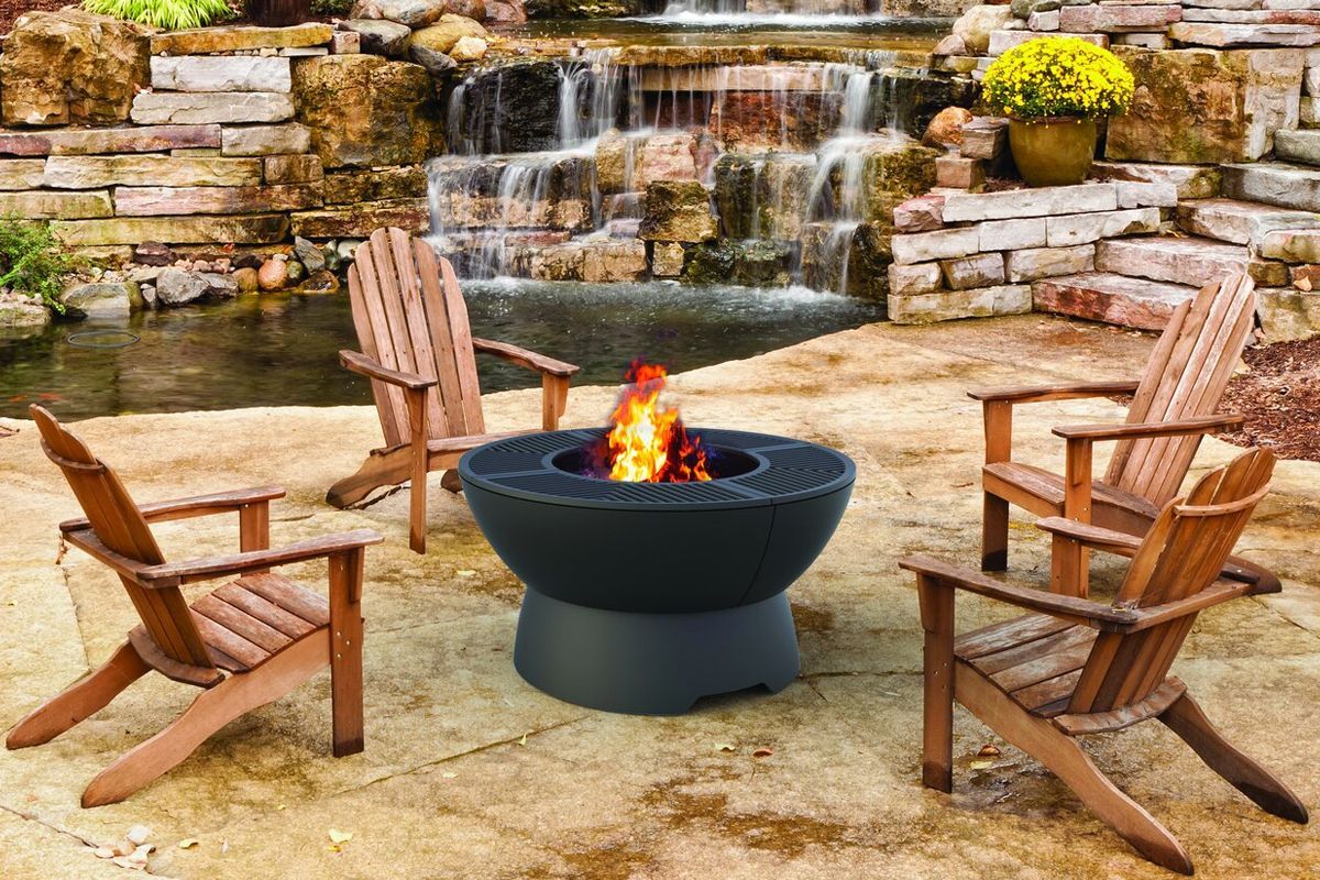 Three wooden chairs circle a fire pit on a patio, with a waterfall and stone wall in the background.