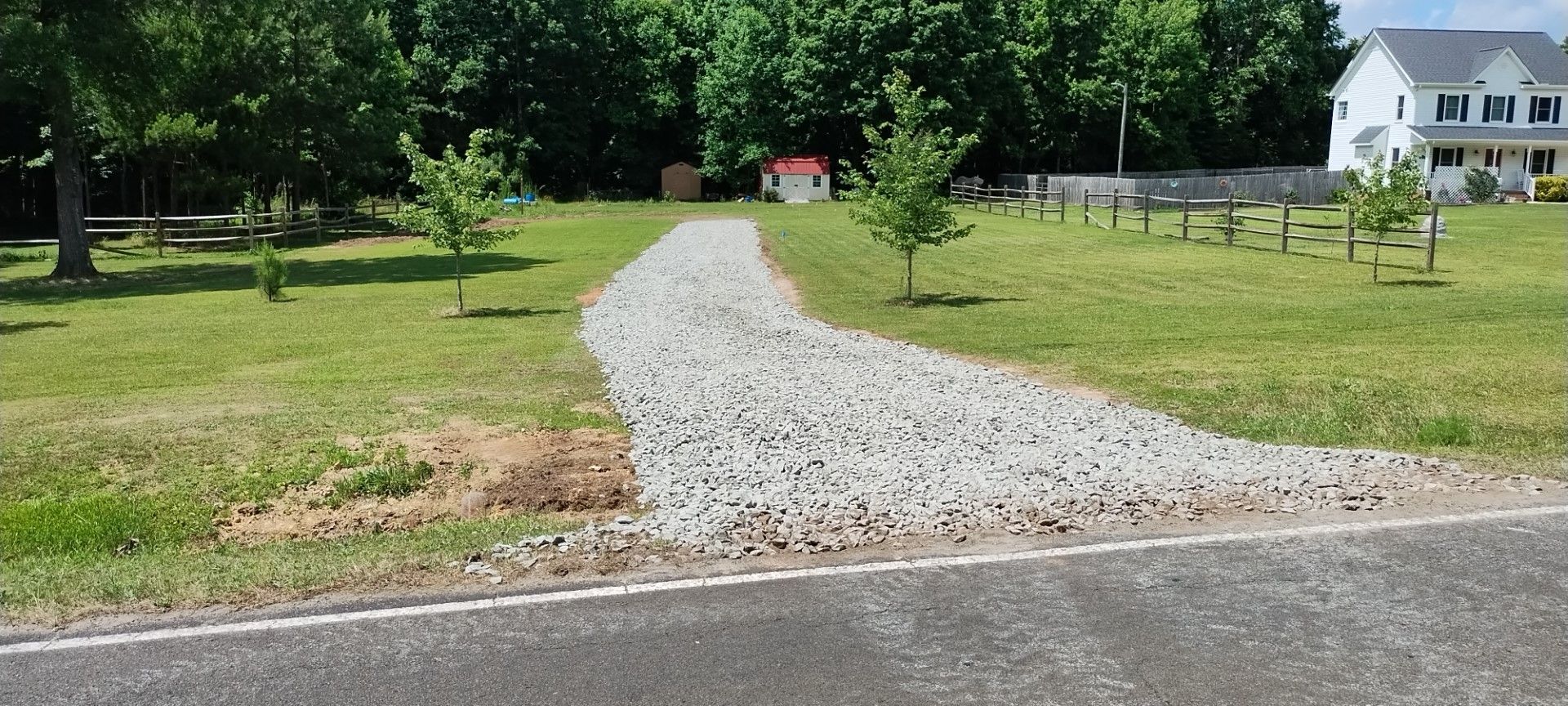 A gravel driveway leading up to a small red-roofed building with a white house in the background.