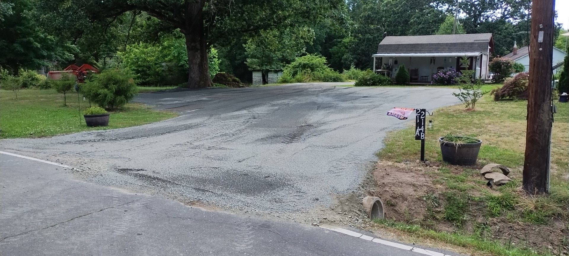 A gravel driveway leading to a house with a porch, mailbox on the right, and a tree in the background.