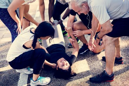 People helping a person lying on the ground outdoors, with concerned expressions
