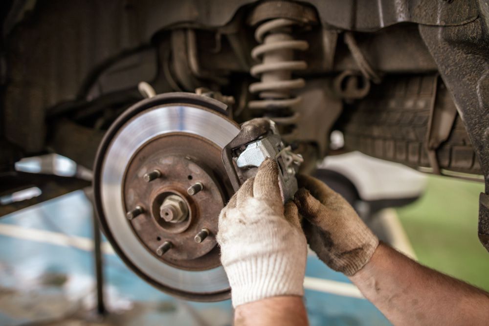 A Person is Fixing a Brake Pad on a Car — Protec Mechanical Repairs In Taree, NSW