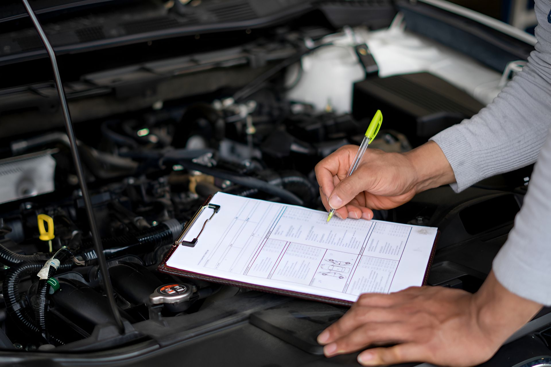 A person is writing on a clipboard in front of a car engine. — Protec Mechanical Repairs In Taree, NSW