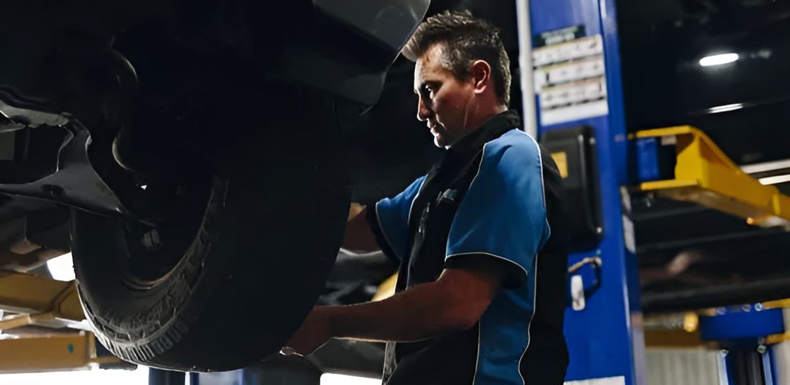 A Man is Repairing a Car on a Lift — Protec Mechanical Repairs In Taree, NSW
