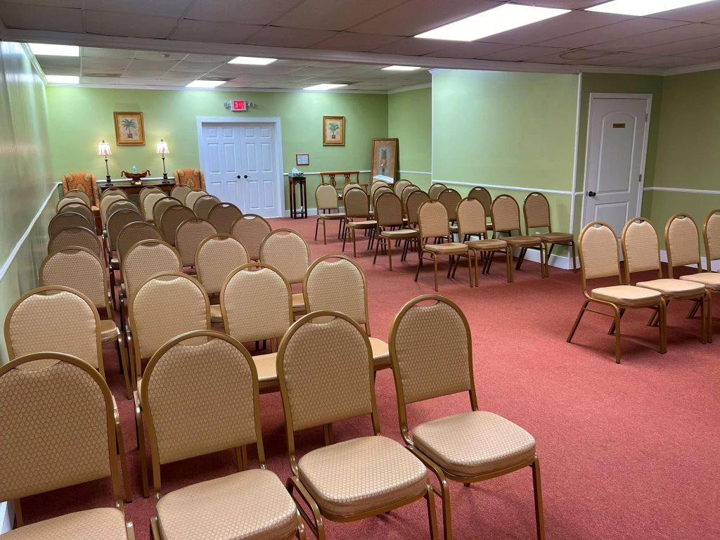 Rows of beige chairs arranged in a room with green walls and red carpet, facing toward a set of double doors.