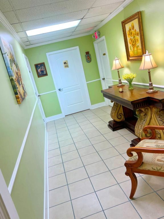 A hallway with light green walls, a tiled floor, two white doors, a wooden console table with two lamps, and an armchair.