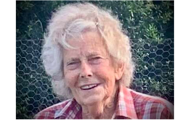 An elderly woman wearing glasses and a floral shirt is smiling for the camera.