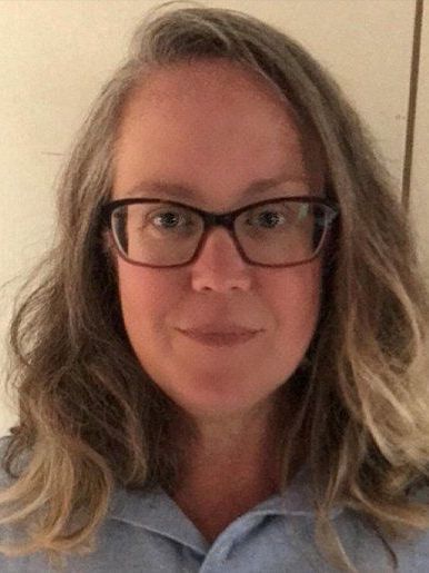 A woman wearing glasses and a blue shirt is smiling for the camera.