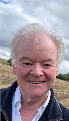 Smiling man outdoors with cloudy sky and hillside in the background