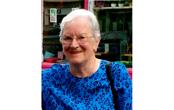 An elderly woman wearing glasses and a floral shirt is smiling for the camera.
