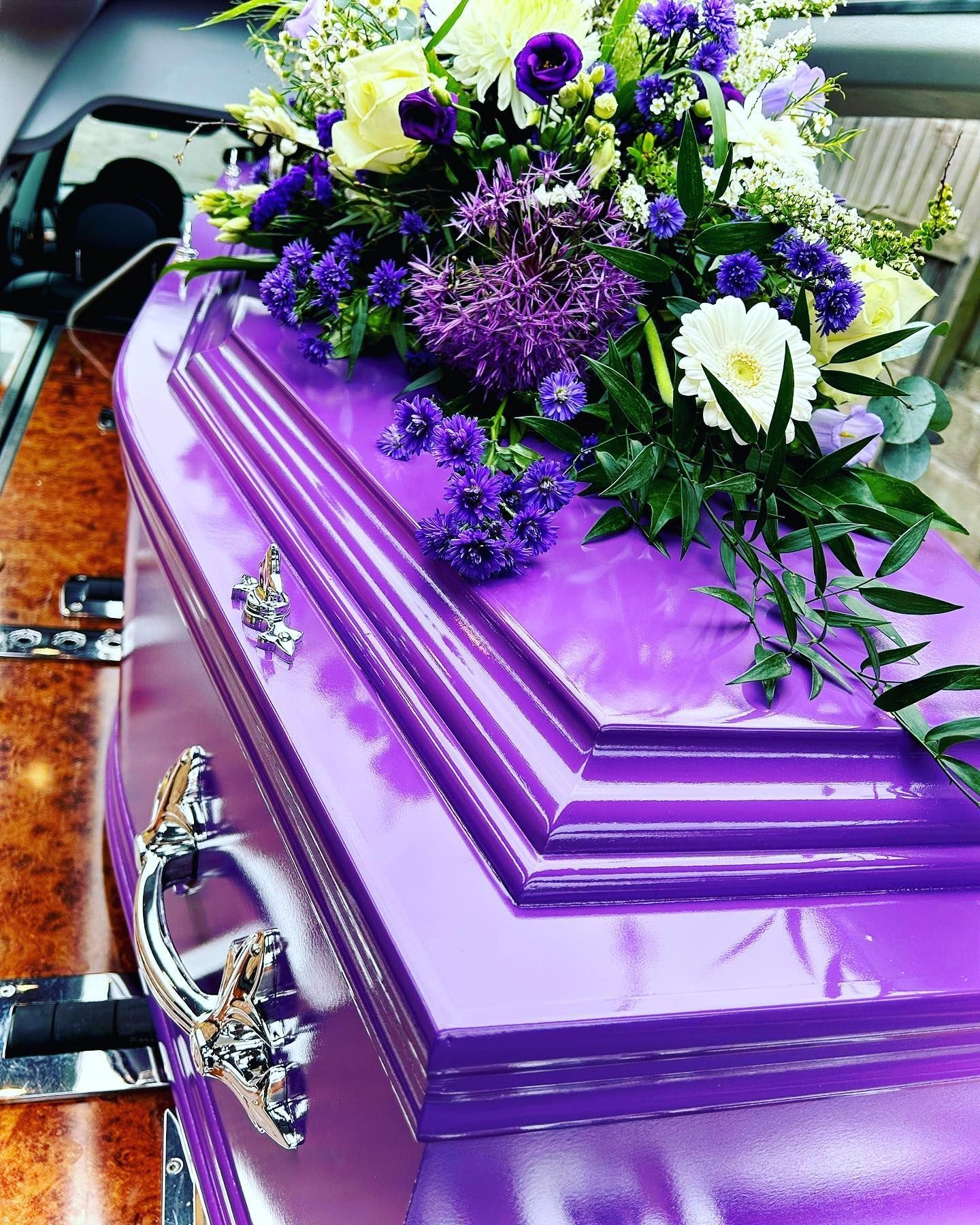 A purple coffin with purple and white flowers on top