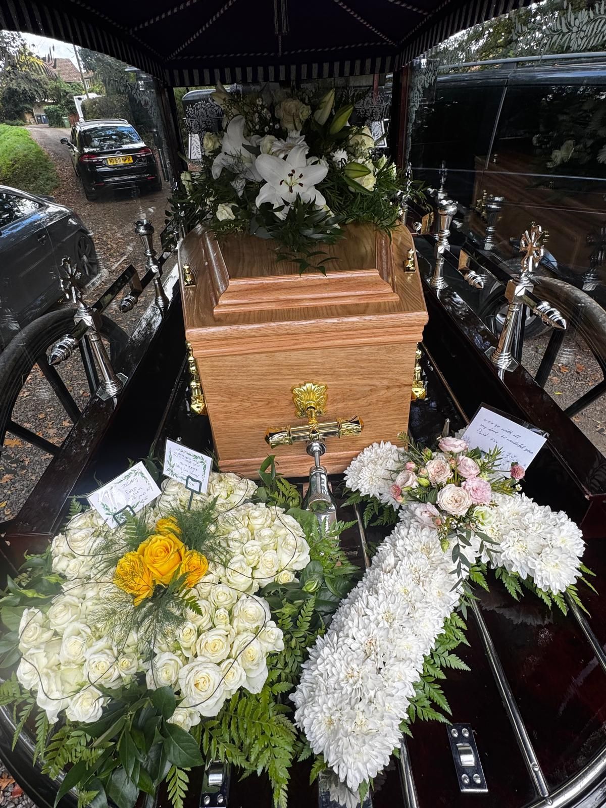 A coffin with floral arrangements inside a hearse, ready for a funeral.