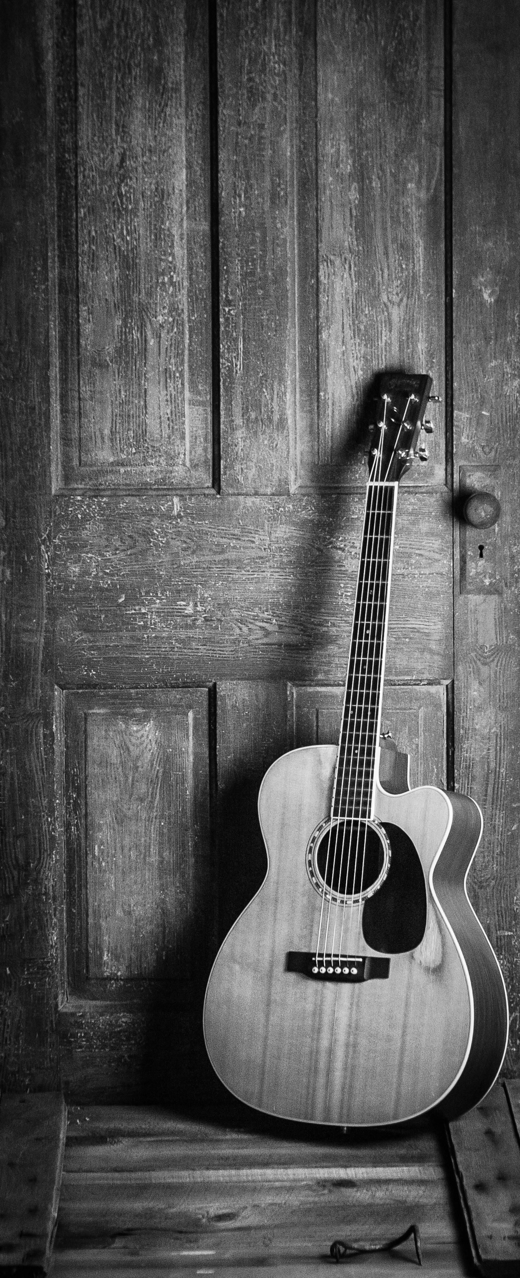 A black and white photo of an acoustic guitar leaning against a wooden door.