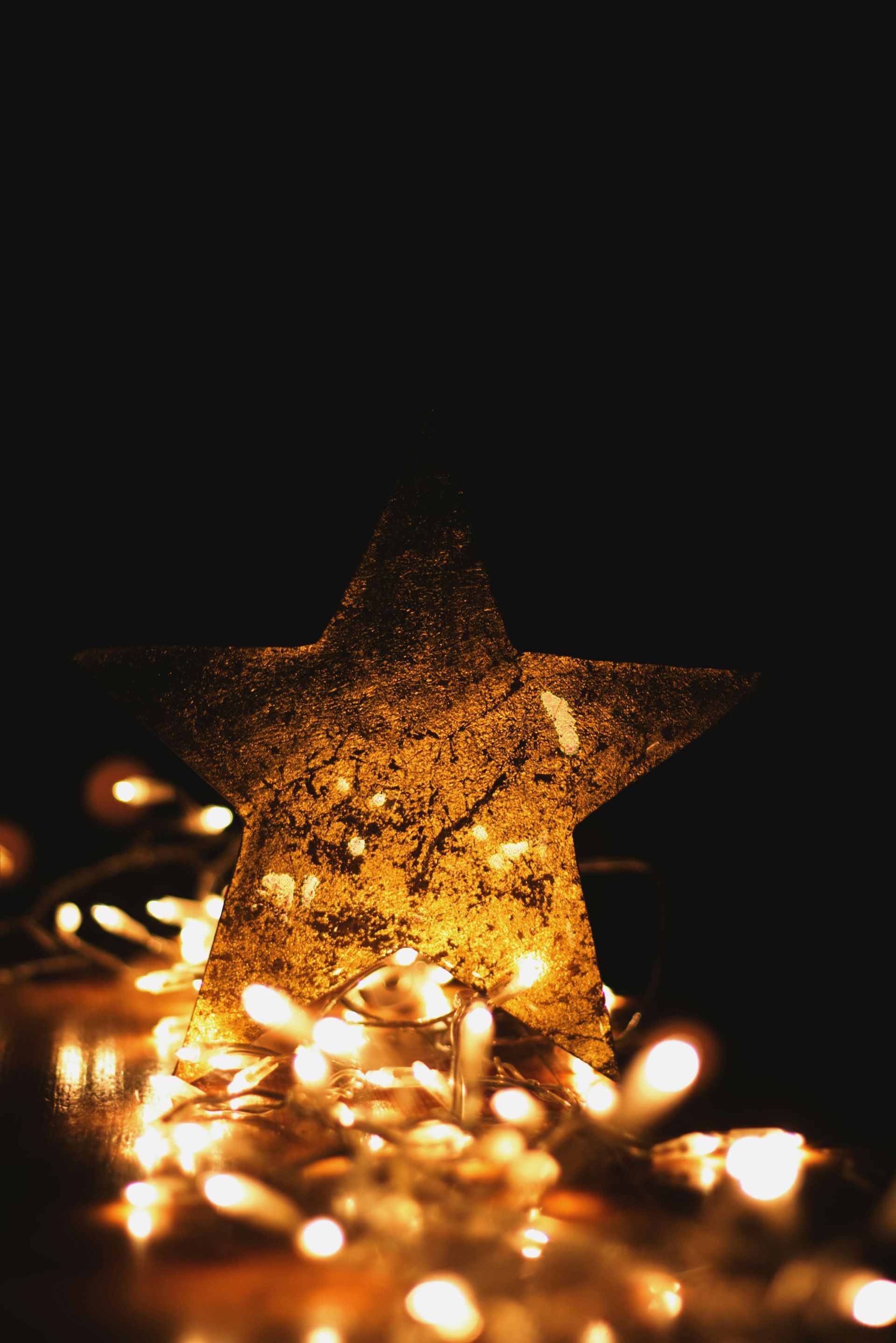 Glittery gold star surrounded by glowing string lights against a dark background.