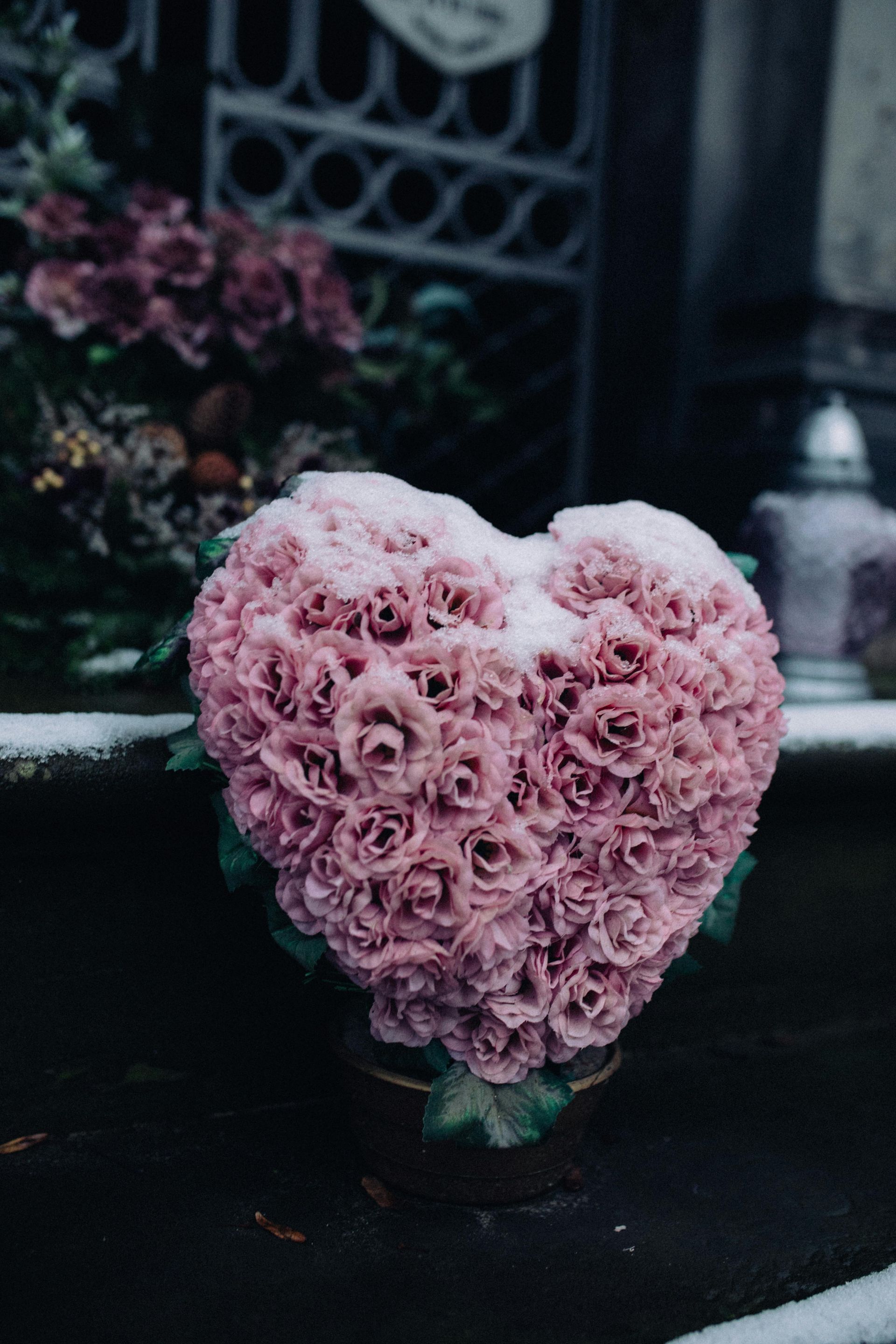 Pink heart-shaped flower arrangement on a dark pedestal, with a softly blurred garden background