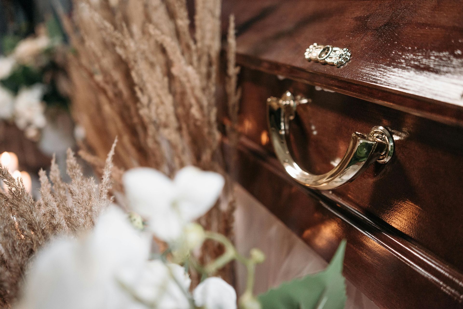 Coffin handle with decorative ring; floral arrangement in the foreground.