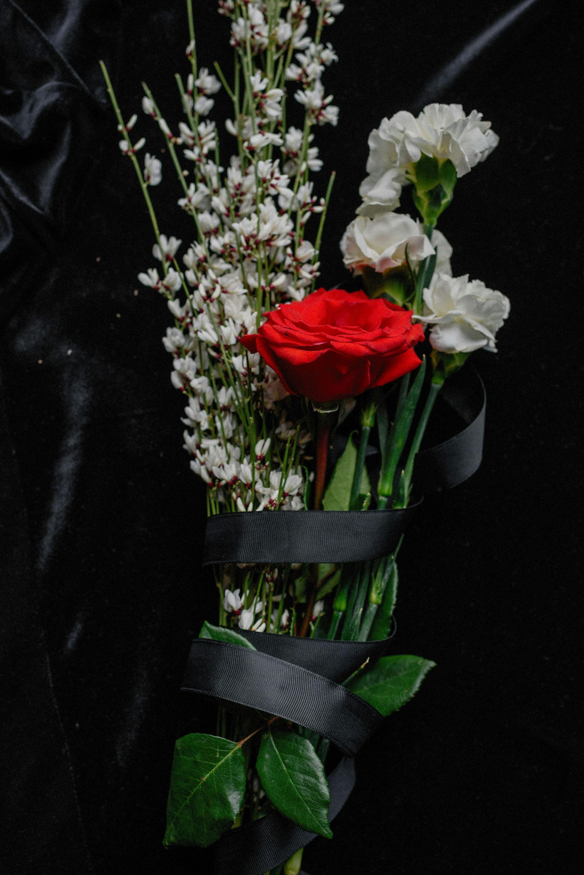 A bouquet of red and white flowers wrapped in dark paper against a black background