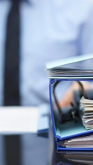 A man in a tie is holding a binder full of papers.