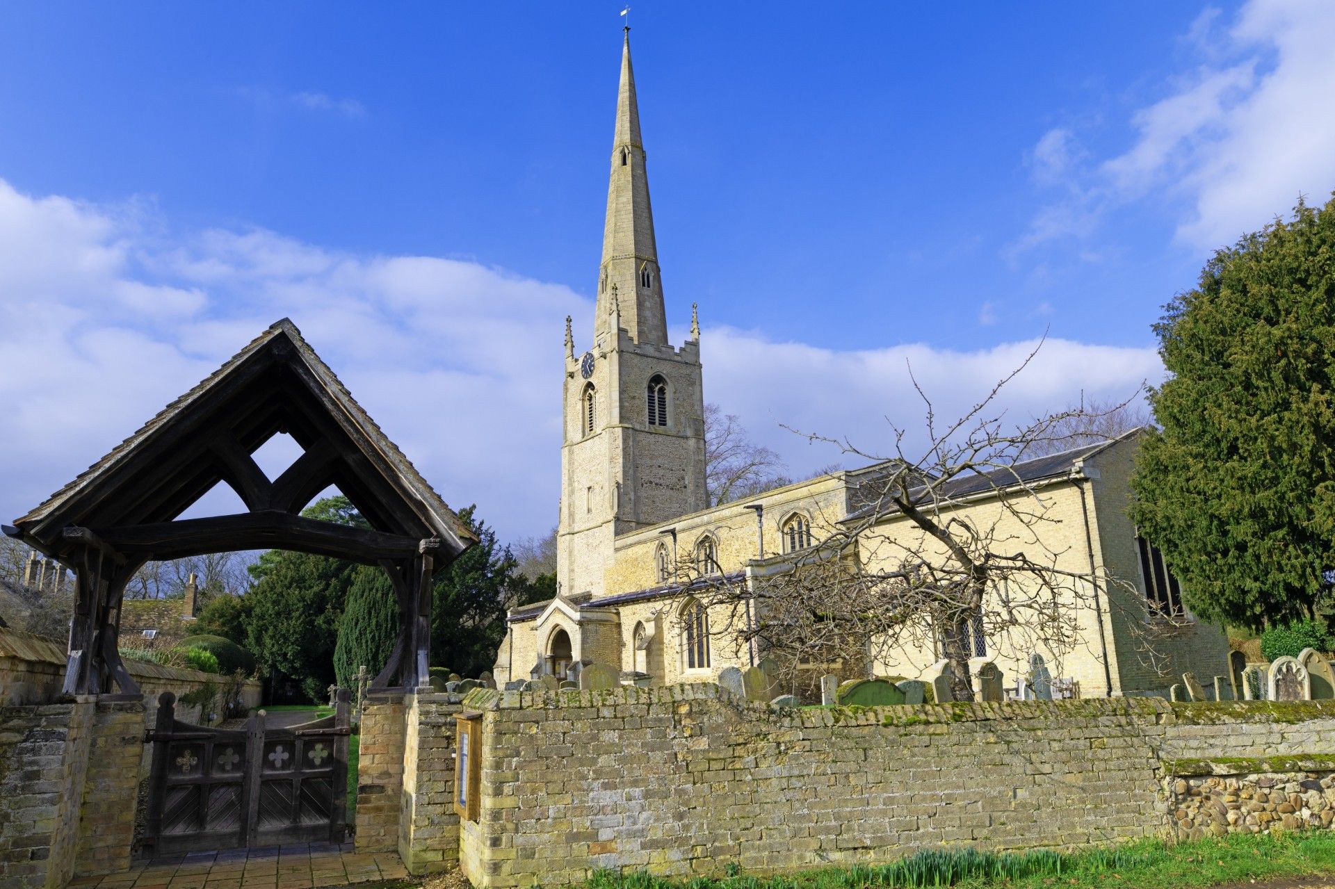 A church with a very tall steeple is surrounded by trees and a stone wall