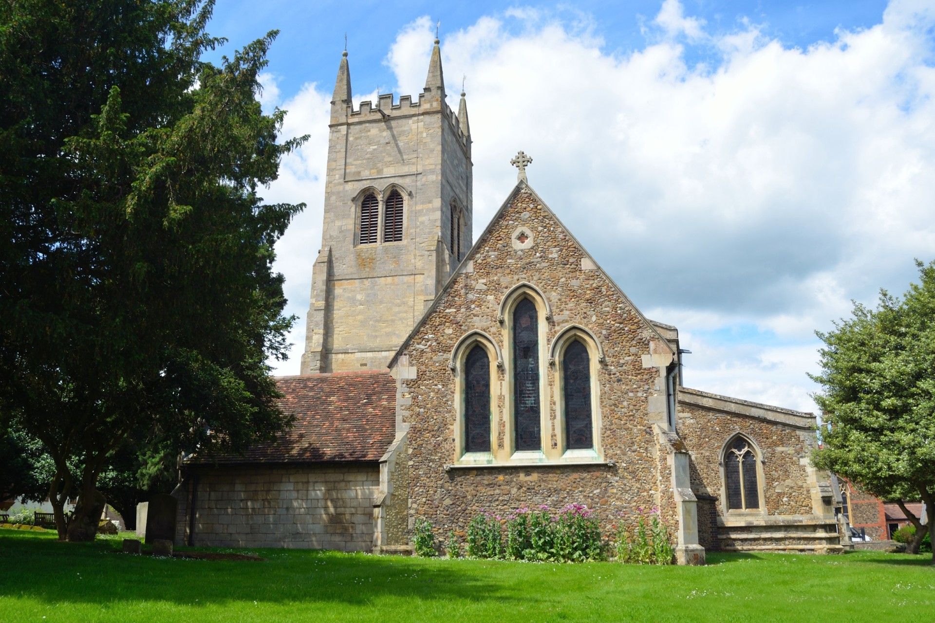 A stone church with a steeple is surrounded by grass and trees