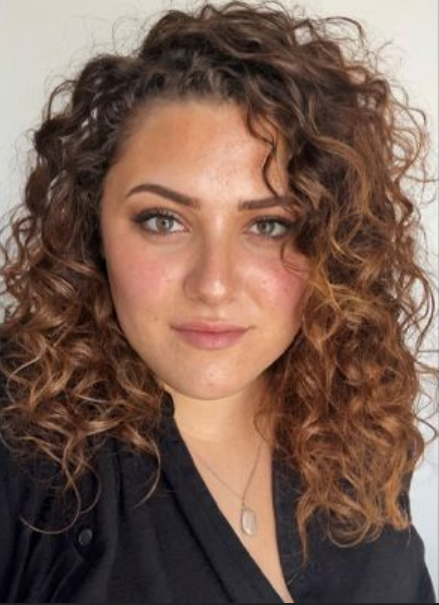 A woman with curly hair is wearing a black shirt and necklace