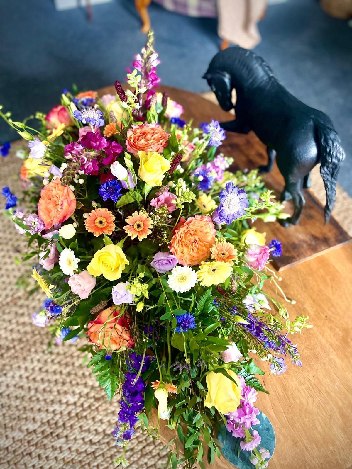 A statue of a horse is sitting on a table next to a bouquet of flowers.