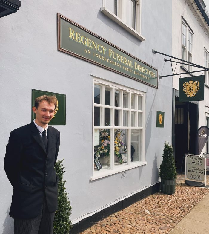 A man in a suit stands in front of a regency funeral directors building