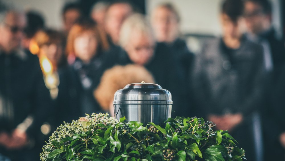 A group of people are standing around a urn at a funeral.