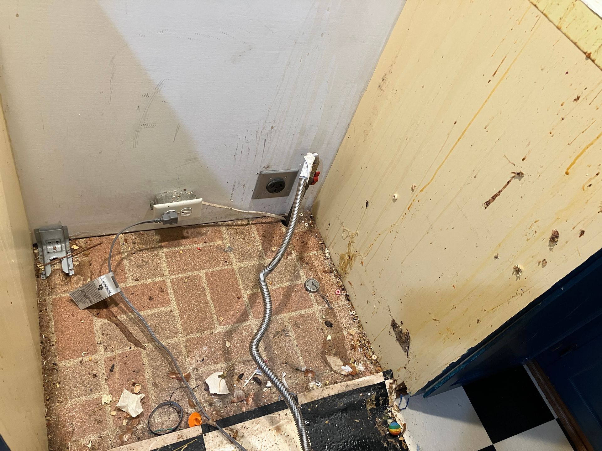 Old food, trash, and gunk behind an oven that has been moved but not cleaned.