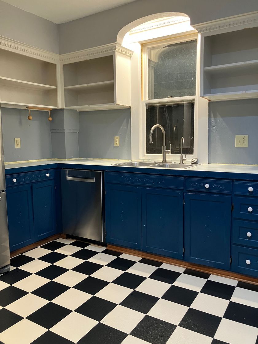 Kitchen with blue cabinets, black-and-white checkered floor, and a tall arched window above the sink.