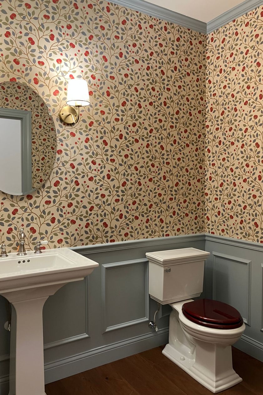 Post Construction clean for small bathroom with floral wallpaper, white sink, and toilet with red seat under a wall sconce.