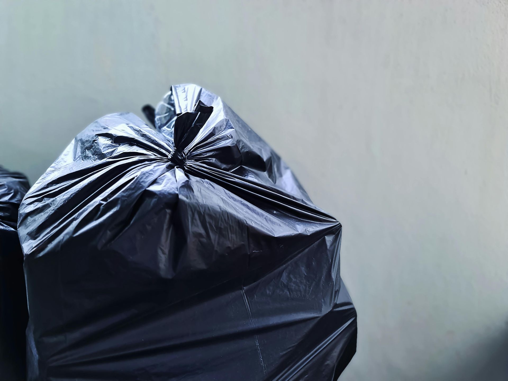 Black garbage bag tied at the top against a plain light-gray wall