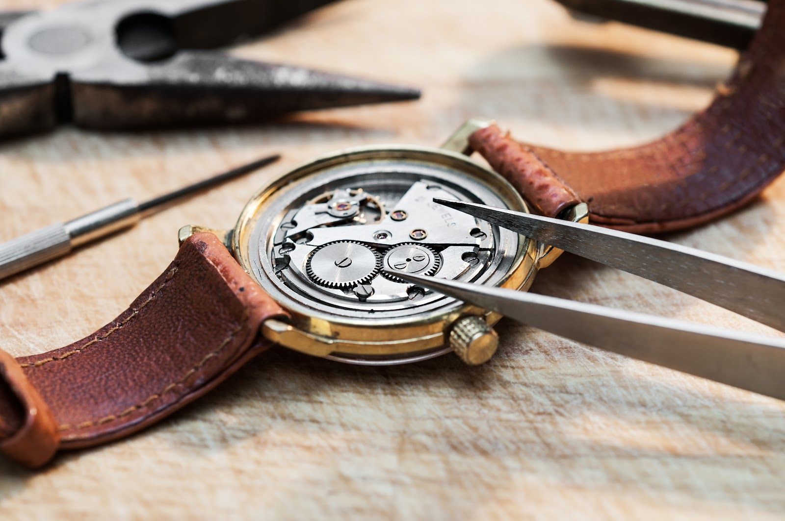 Watchmaker repairing a wristwatch with tweezers on a workbench