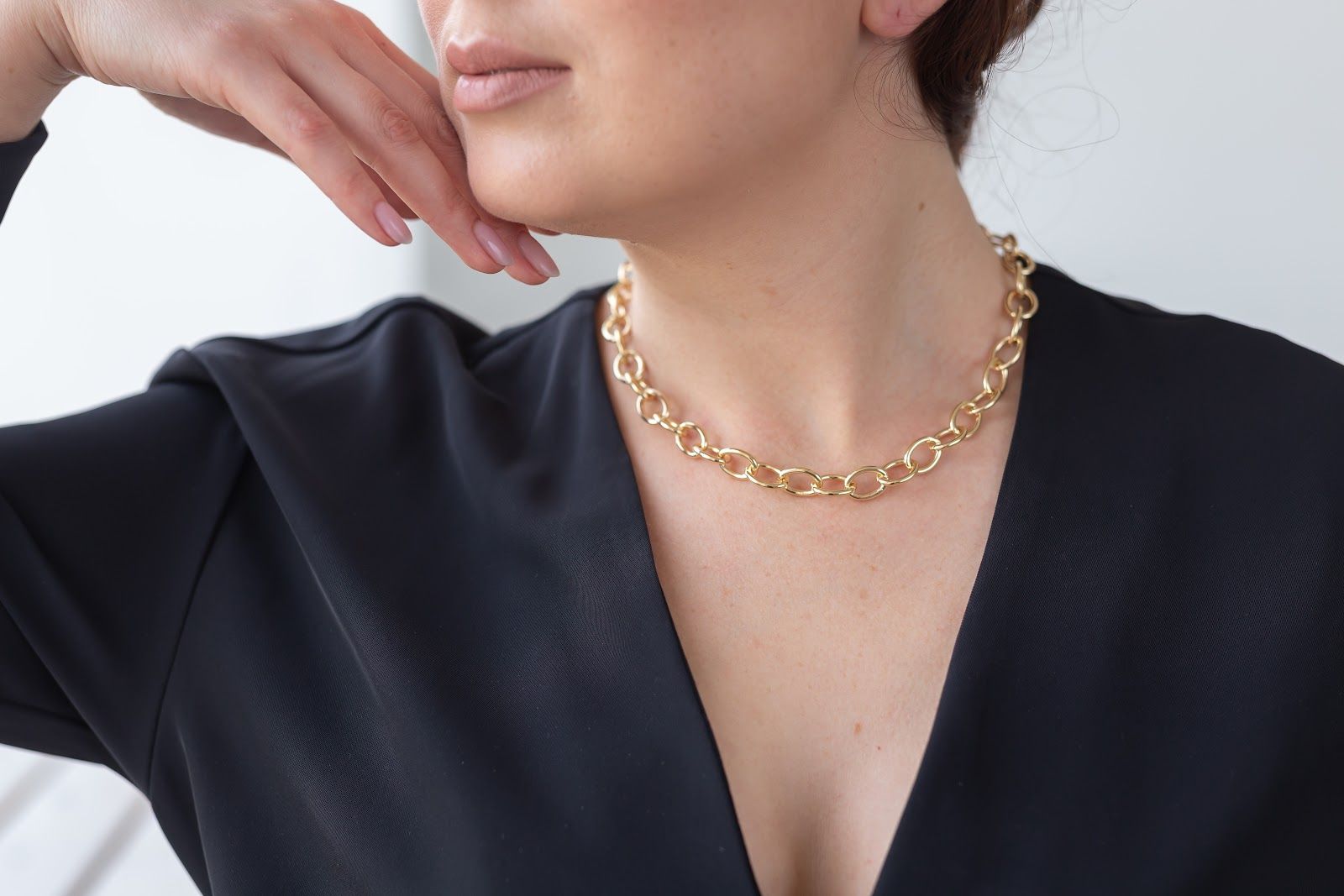 Close-up of a person wearing a gold chain necklace and black V-neck top, hand resting near the chin