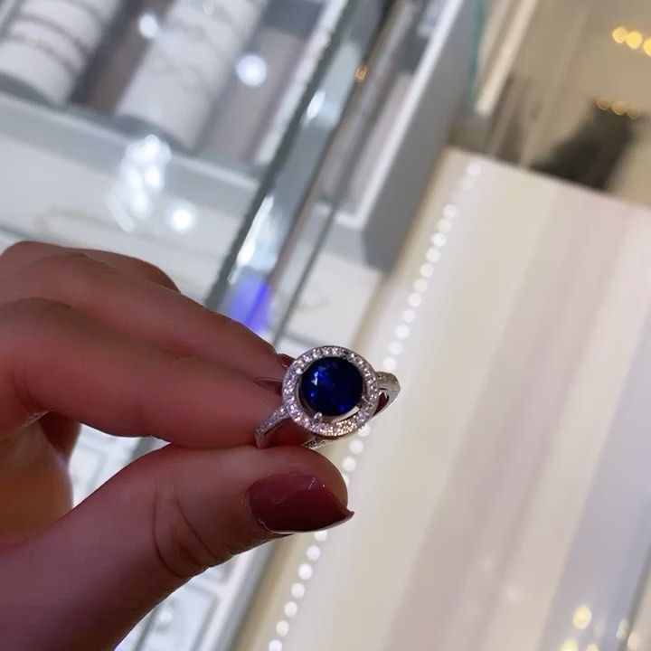 A person is holding a ring with a blue stone in the center