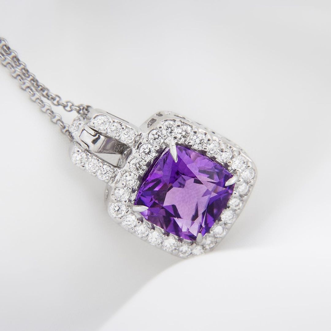 A necklace with a purple stone and diamonds on a white surface.