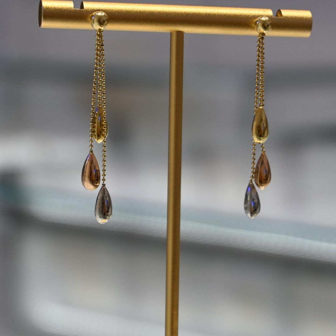 A pair of earrings are sitting on a gold stand.