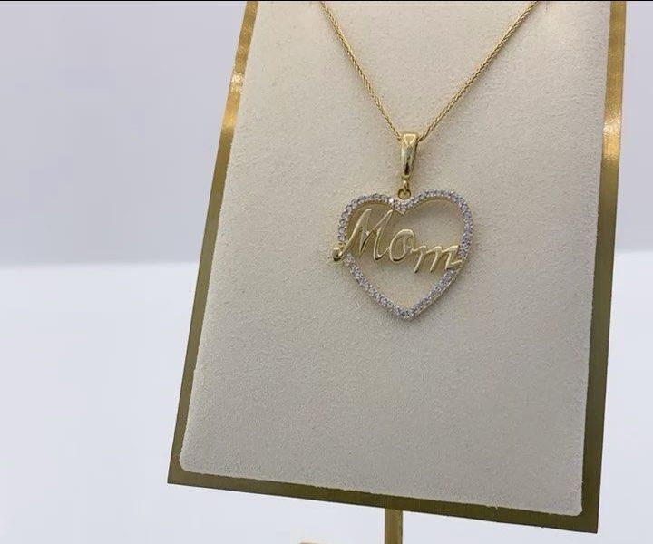 A gold necklace with a heart shaped pendant that says mom