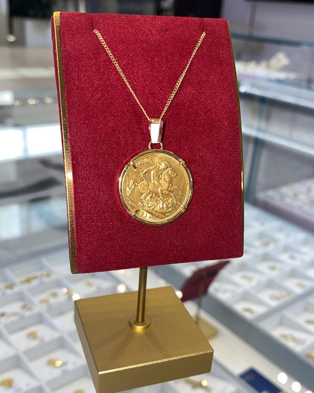 A gold coin necklace is displayed on a gold stand