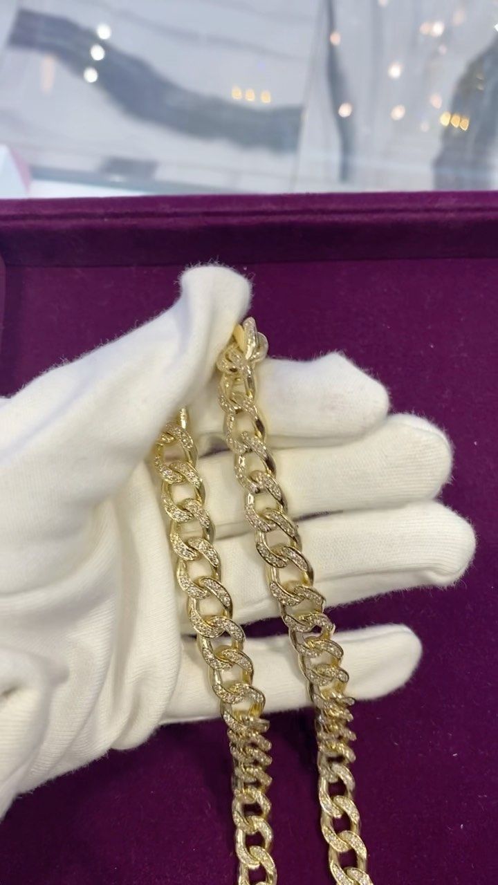 A person wearing white gloves is holding a gold chain